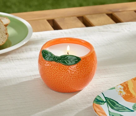 Płonąca świeca citronella w pomarańczowym pojemniku na stole.