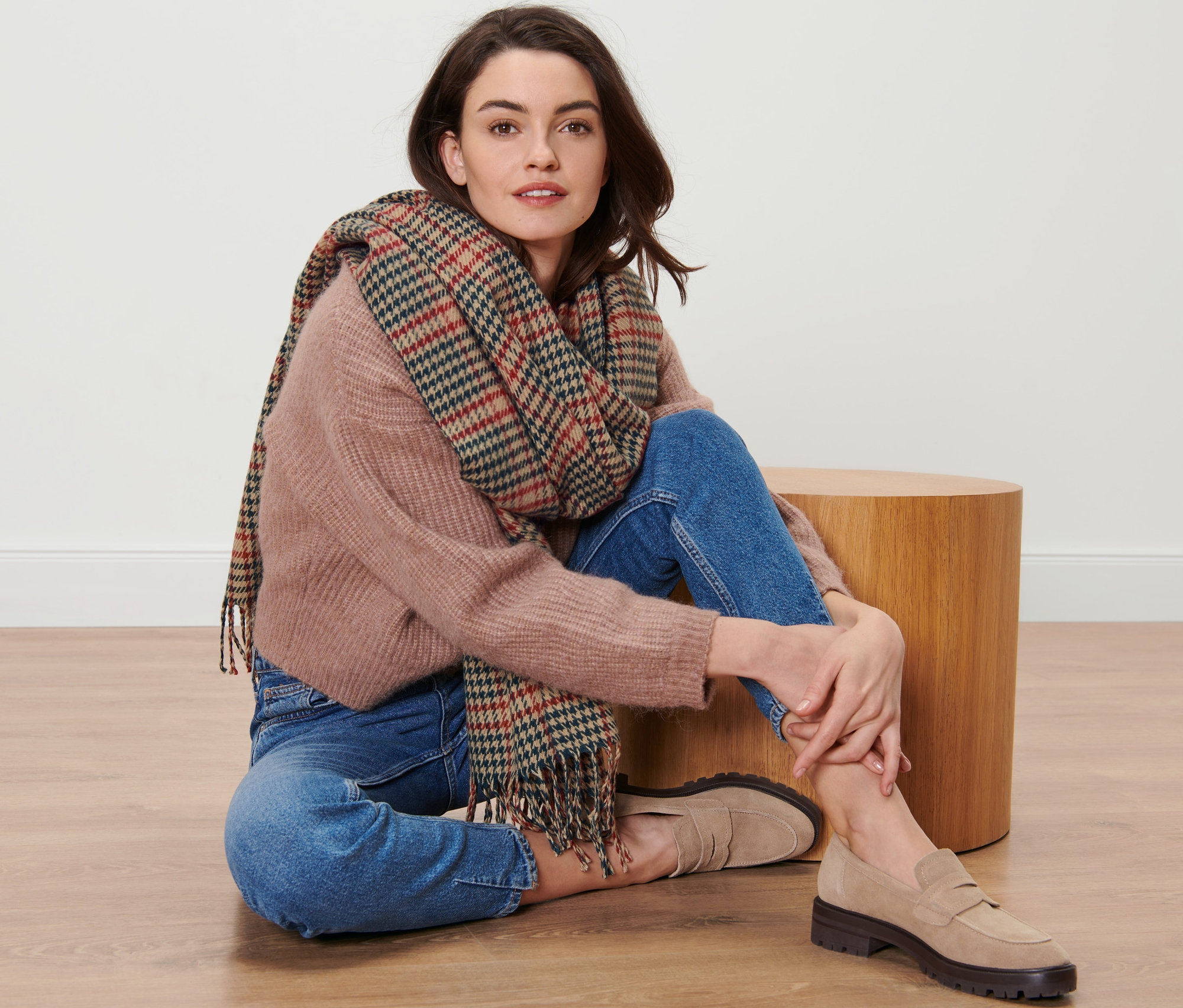 Kobieta siedzi na podłodze w tkanym szalu w kratkę.