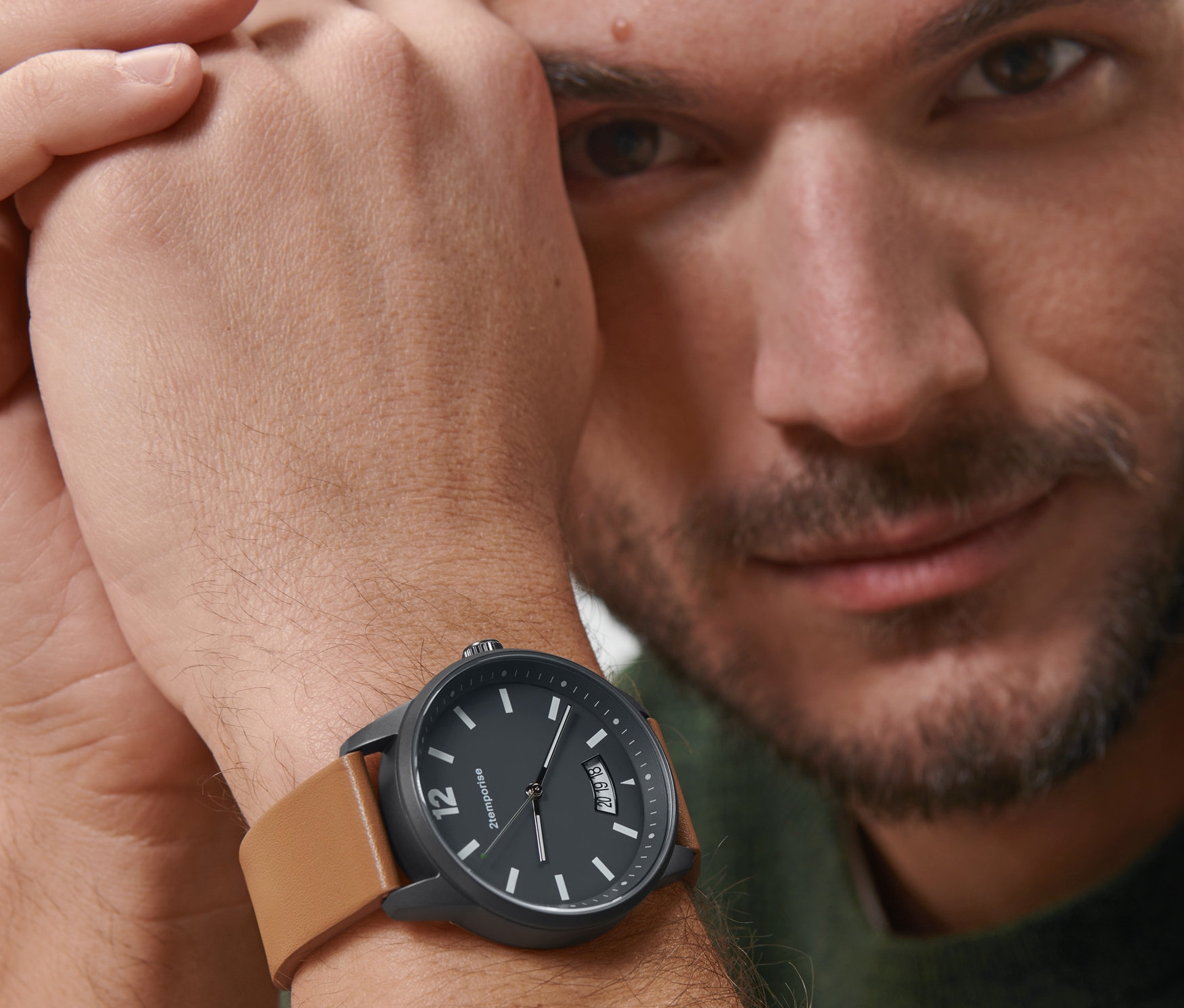 Mężczyzna patrzy w kamerę i nosi na nadgarstku czarny zegarek na rękę Pilot Style Date z brązowym skórzanym paskiem.