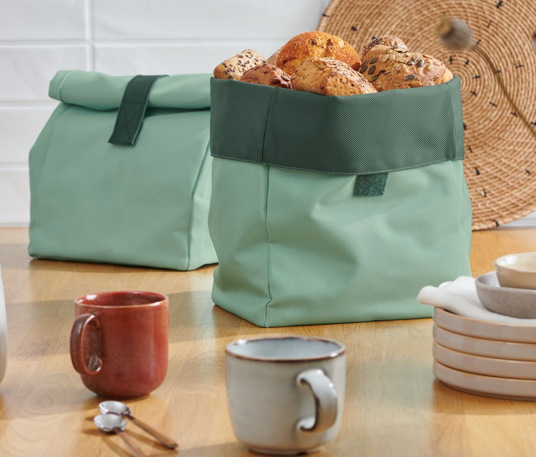 Dwa zielone worki na pieczywo 2 w 1 stoją na drewnianym stole.