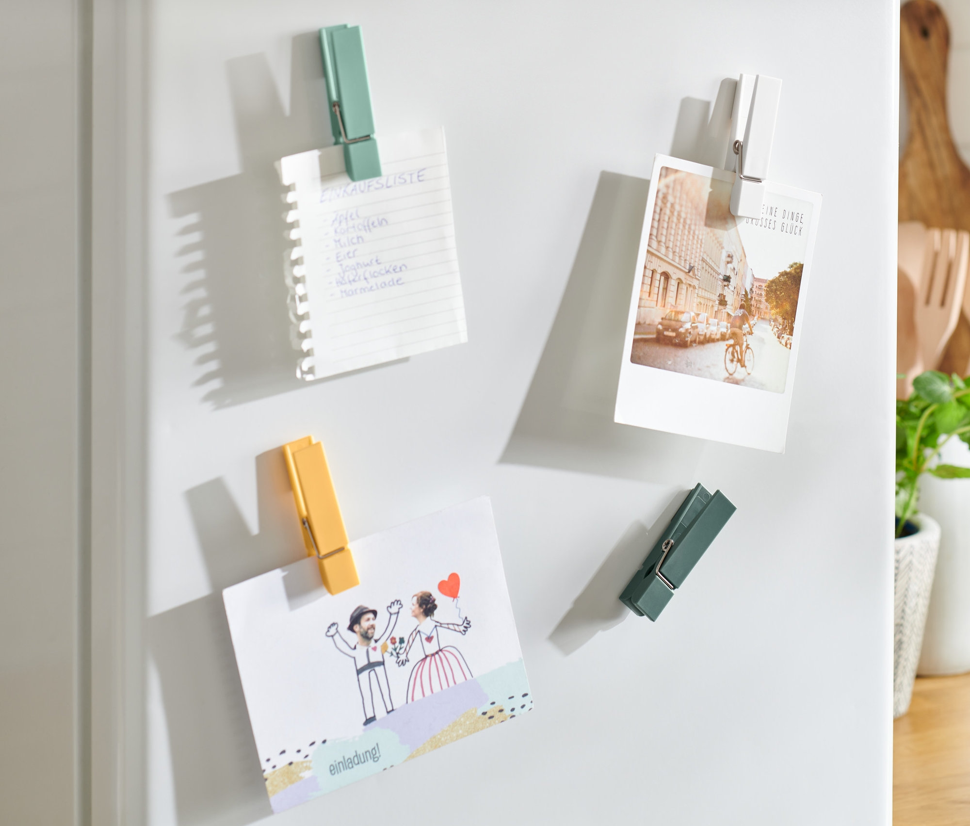 Na białej lodówce przymocowane są magnesy na lodówkę (4 sztuki), przytrzymujące listę zakupów, zdjęcie i zaproszenie ślubne.