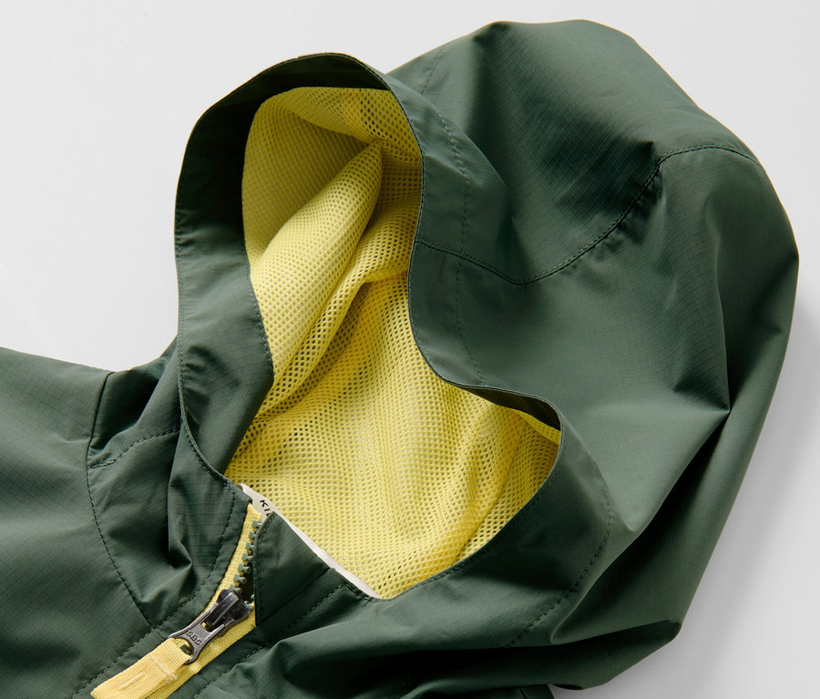 Zbliżenie na zieloną sportową kurtkę funkcyjną dla dzieci z kapturem i żółtym zamkiem błyskawicznym.