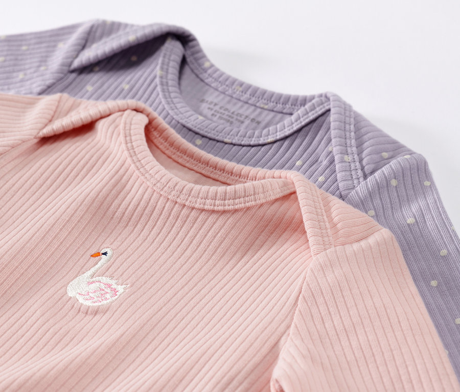 Zbliżenie na dwie koszulki niemowlęce z długim rękawem o prążkowanej fakturze w kolorze różowym i fioletowym. Różowa koszulka ma haft z łabędziem.
