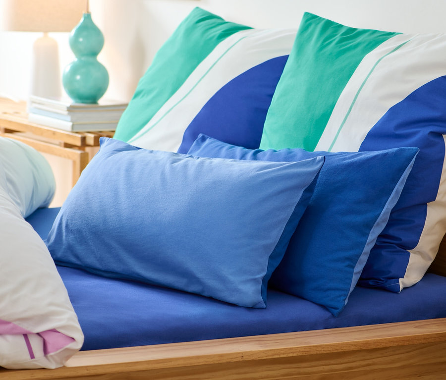 Dwie dżersejowe poszewki na poduszki leżą na łóżku z niebieskim prześcieradłem.
