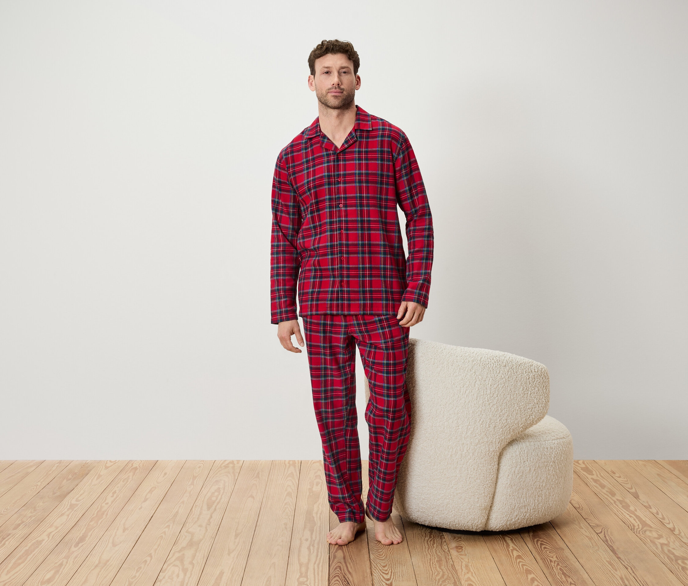 Mężczyzna w czerwonej piżamie w kratę stoi w pokoju obok białego fotela.