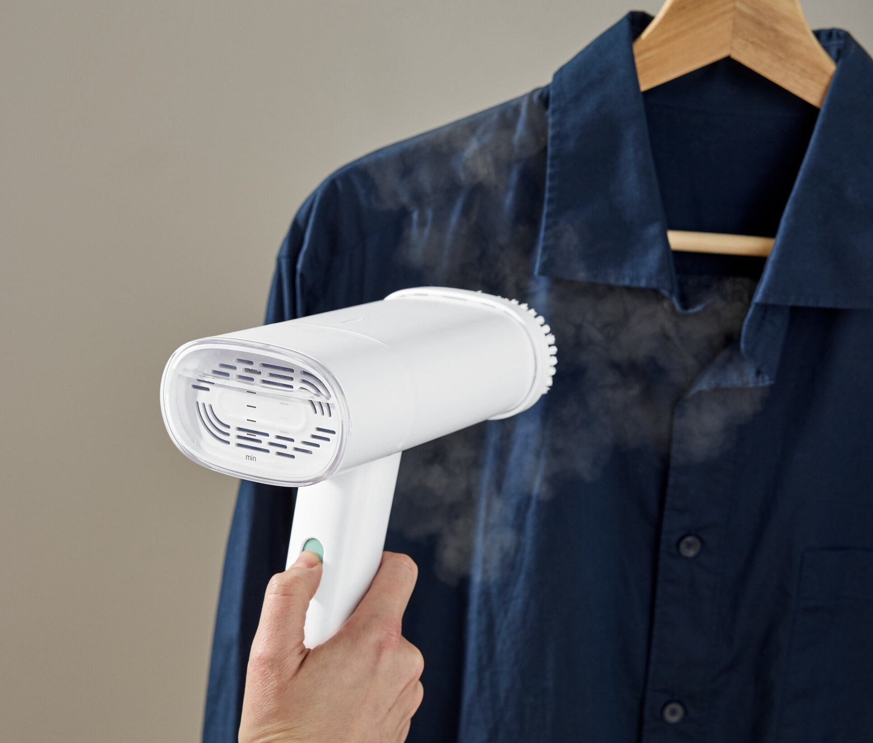 Ręka używa szczotki parowej na granatowej koszuli wiszącej na wieszaku.