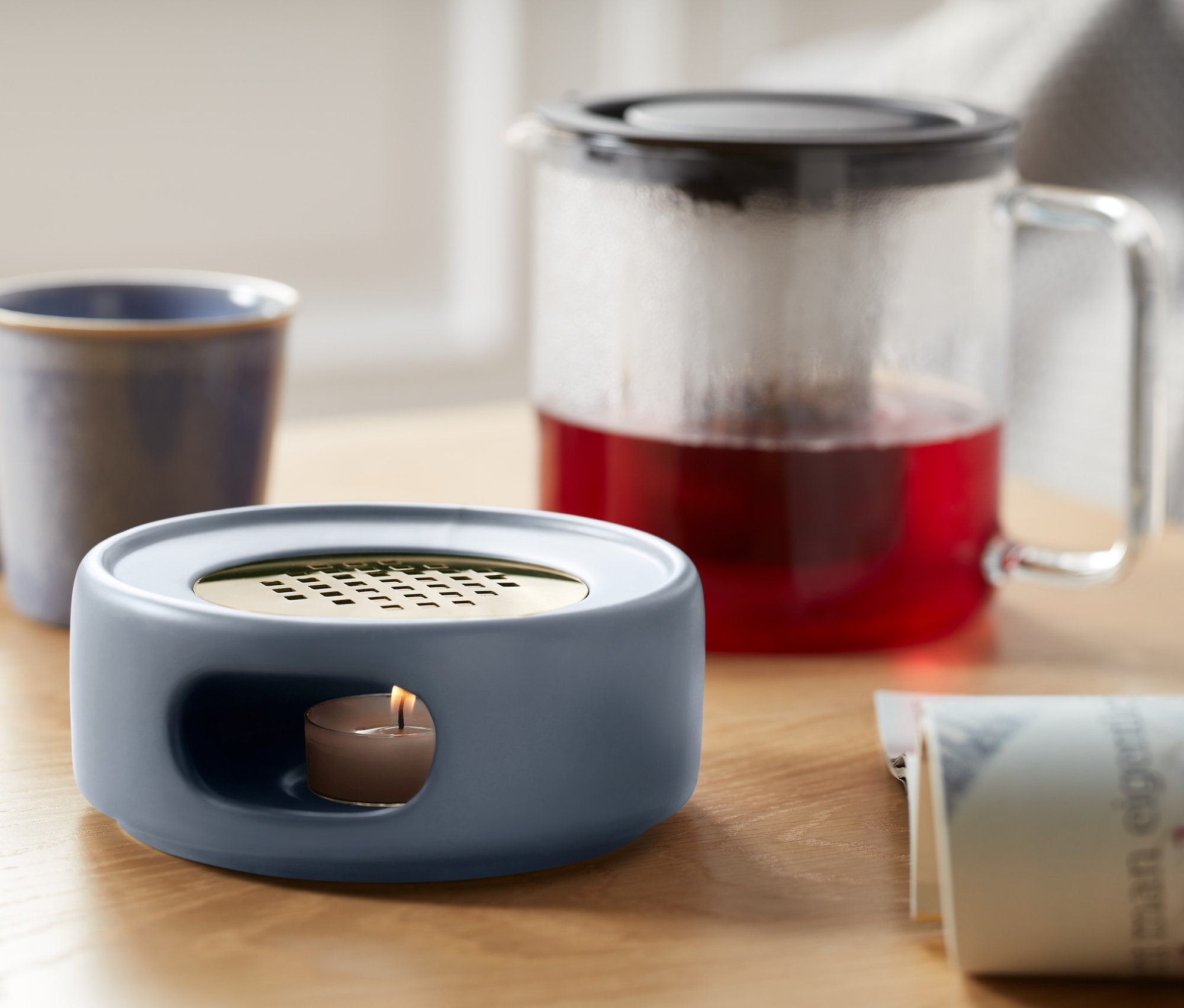 Na stole stoi podgrzewacz, filiżanka i dzbanek z herbatą.