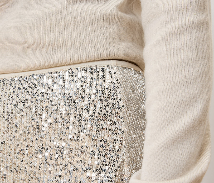 Szczegół damskiego stroju: kremowy sweter i srebrna spódnica cekinowa.