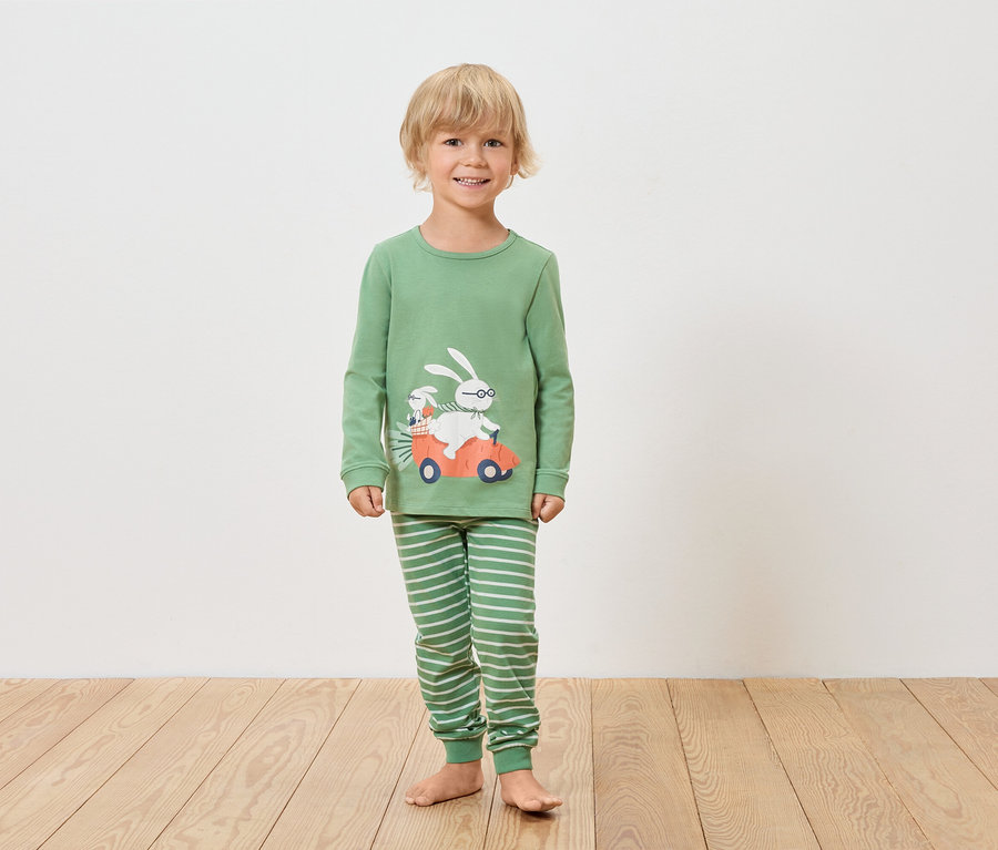 Chłopiec w zielonej piżamie z długim rękawem i pasiastych spodniach z motywem królika w samochodzie.