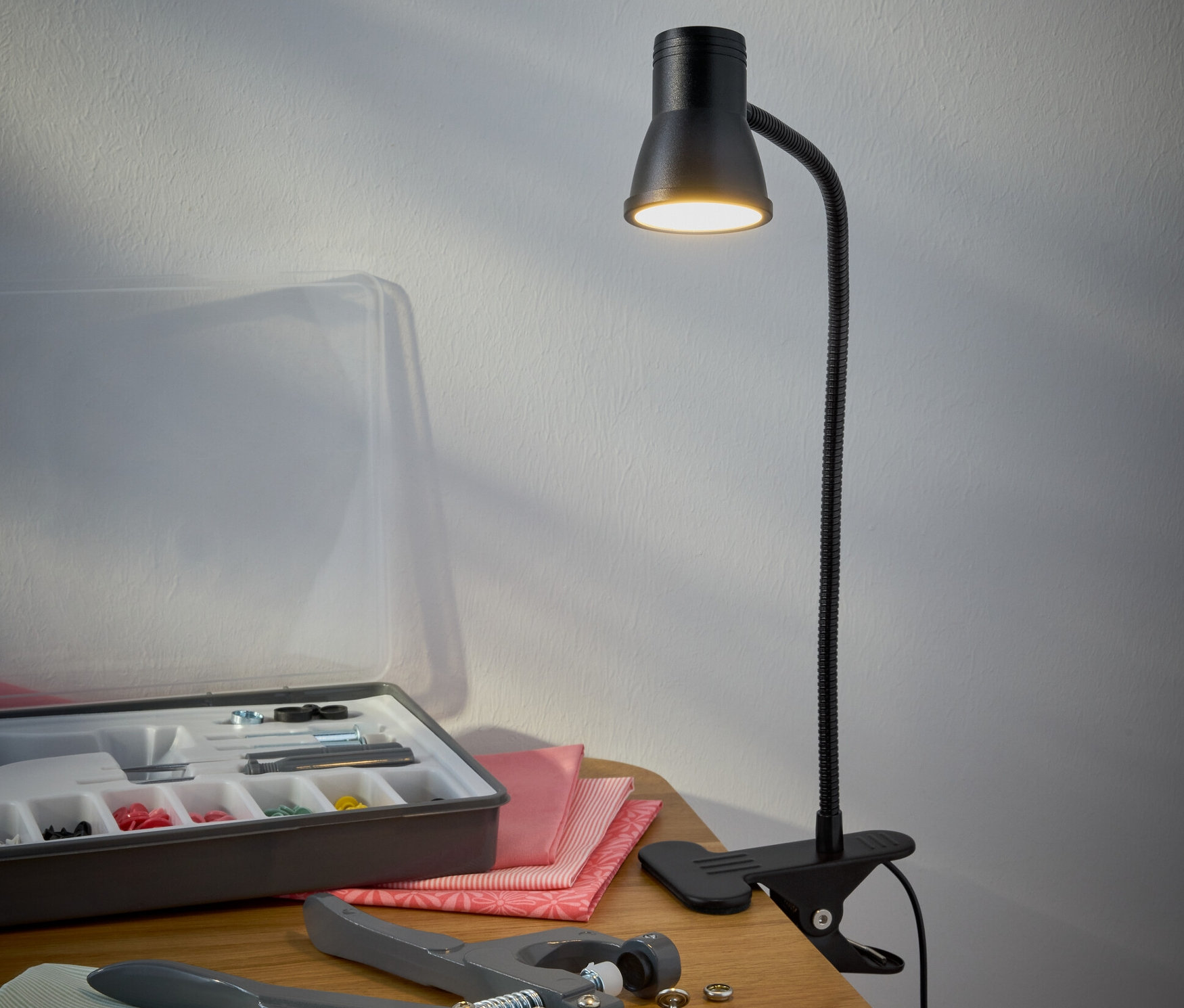 Czarna lampa LED z klipsem stoi na stole obok zestawu do szycia.