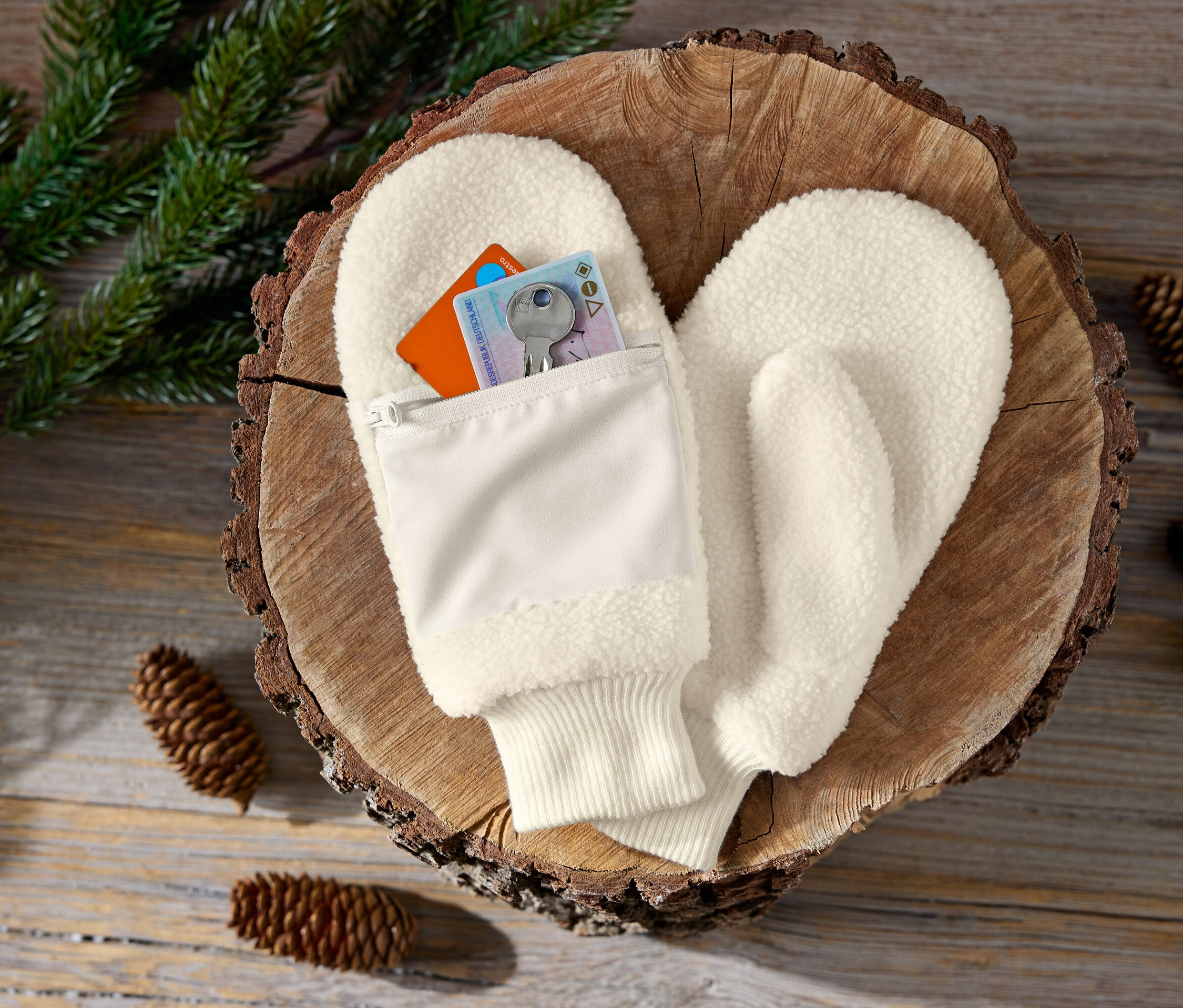 Kremowe rękawice z kieszenią na zamek błyskawiczny na drewnianym podłożu z szyszkami i gałązkami.