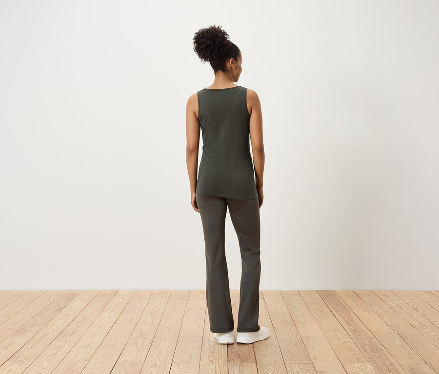 Kobieta stoi tyłem do kamery, ubrana w podkoszulkę i spodnie.