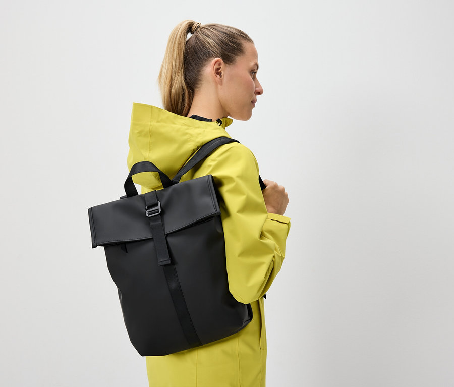 Kobieta z blond włosami związanymi w kucyk ma na sobie żółtą kurtkę i czarny plecak.