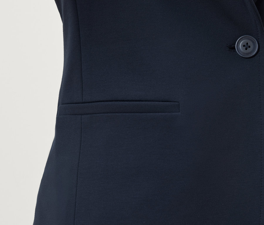 Szczegół granatowej marynarki z guzikiem i kieszenią.