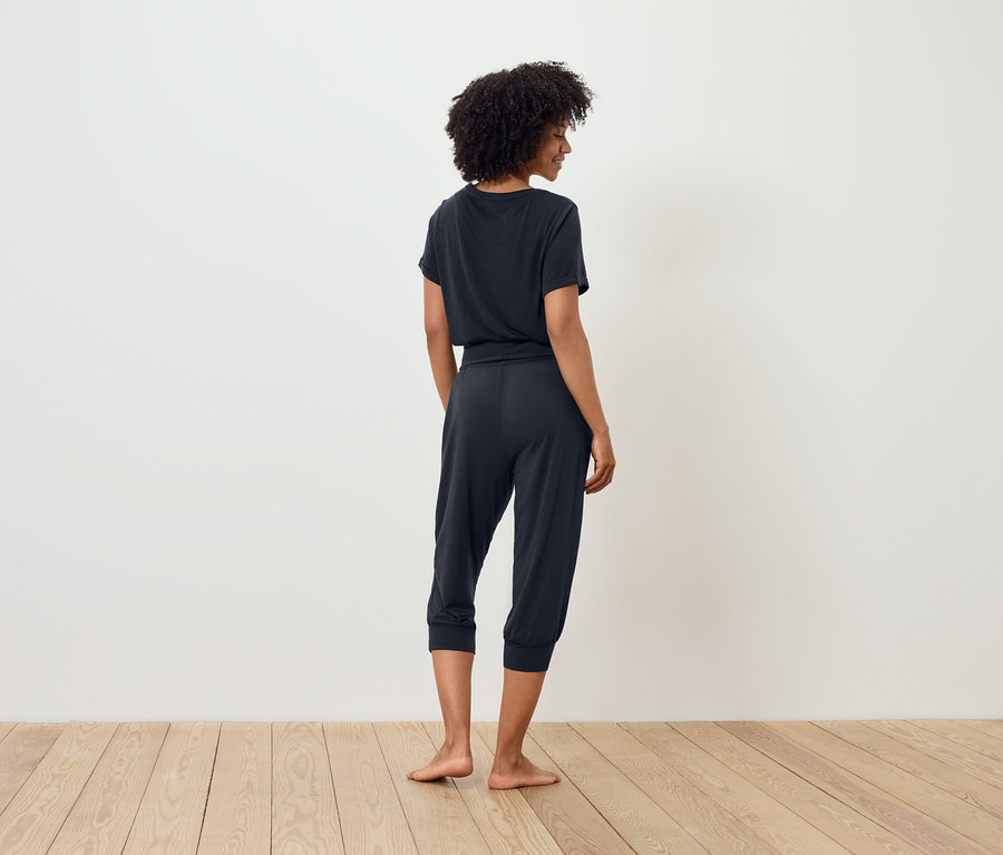 Kobieta w ciemnym t-shircie i spodniach trzy czwarte stoi tyłem do kamery.