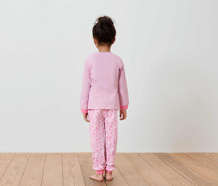 Dziewczynka w różowej piżamie stoi tyłem do aparatu.