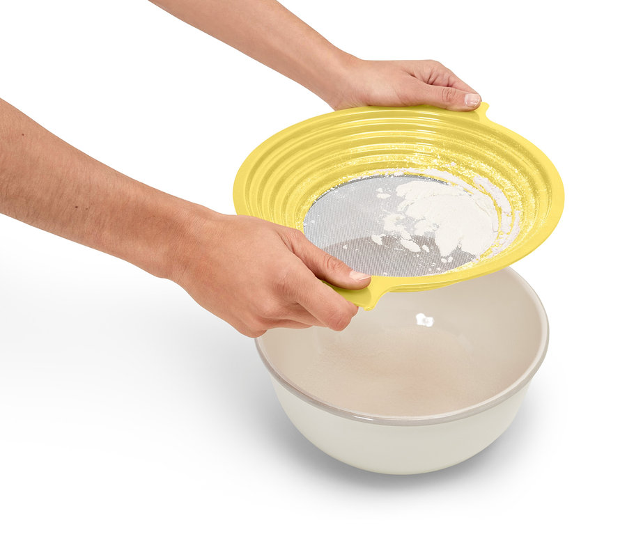 Osoba trzyma żółte sito nad miską i przesiewa mąkę.