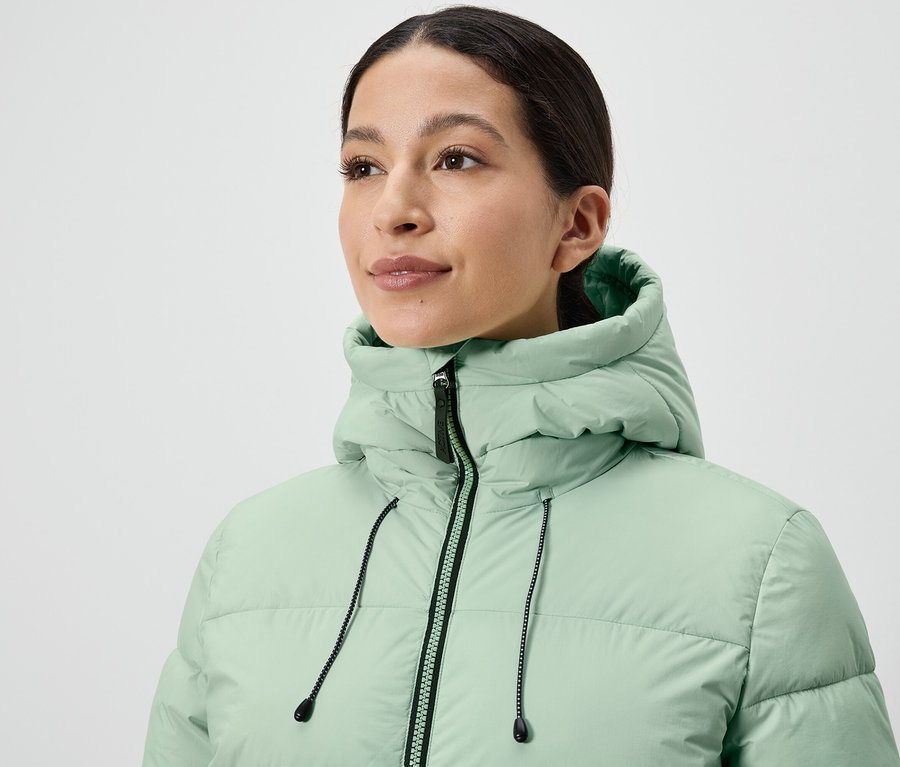 Kobieta ma na sobie jasnozieloną kurtkę puchową.