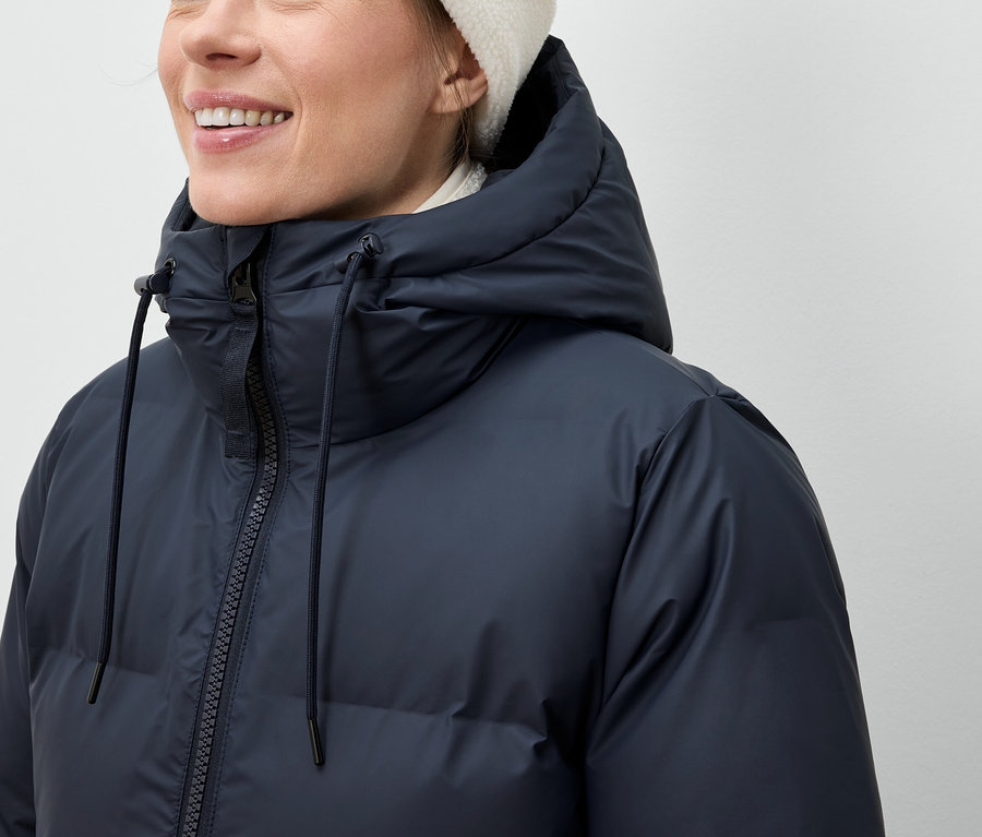 Kobieta ma na sobie granatową kurtkę puchową i białą czapkę.