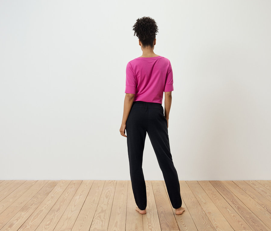 Kobieta tyłem do kamery ma na sobie różową koszulkę i czarne spodnie.