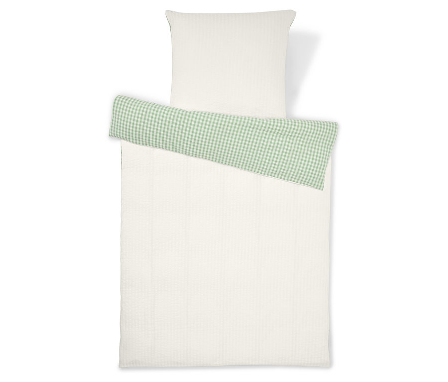 Zestaw pościeli składający się z białej poszewki na poduszkę i białej poszwy na kołdrę z zielonym, kraciastym detalem.
