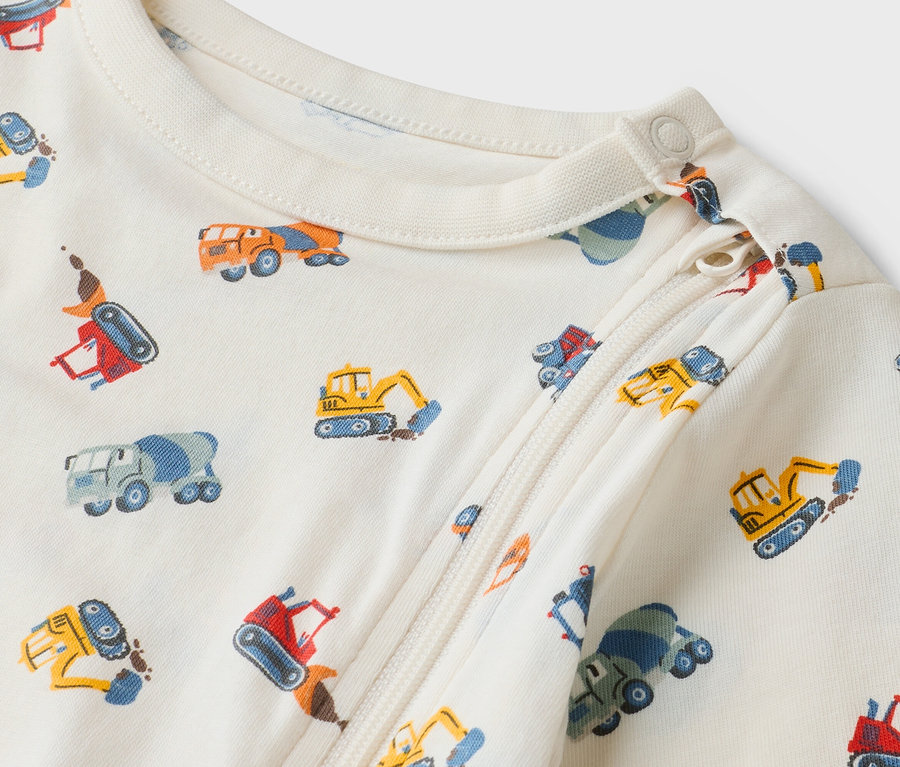 Zbliżenie kremowego pajacyka niemowlęcego z zamkiem błyskawicznym i wzorem w wózki budowlane.