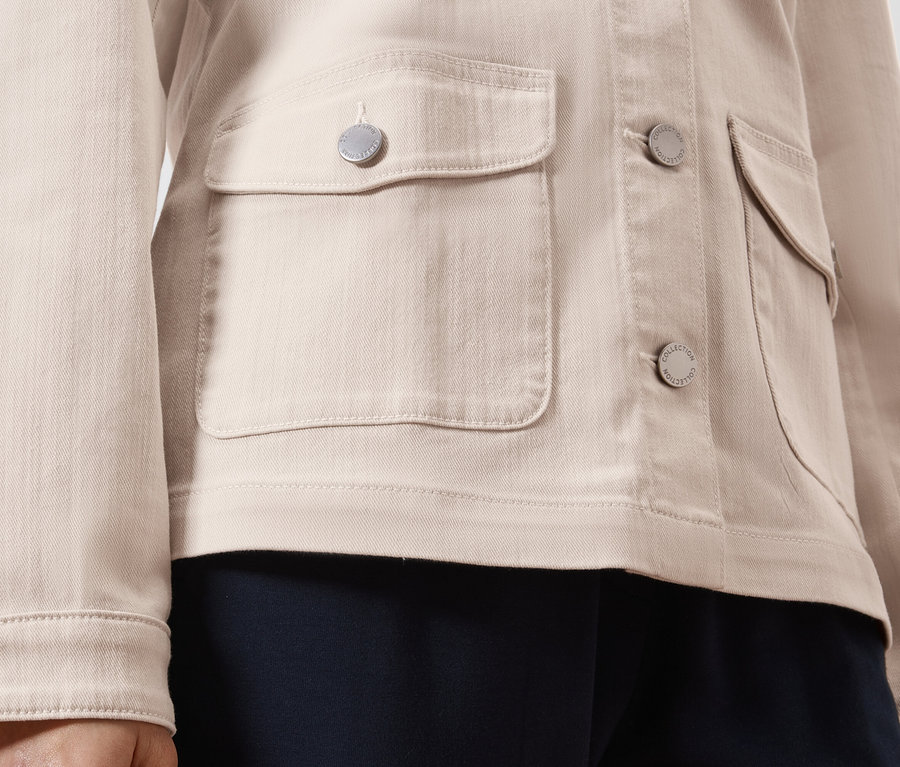 Zbliżenie na jasno-brązową kurtkę jeansową ze srebrnymi guzikami i naszytymi kieszeniami.