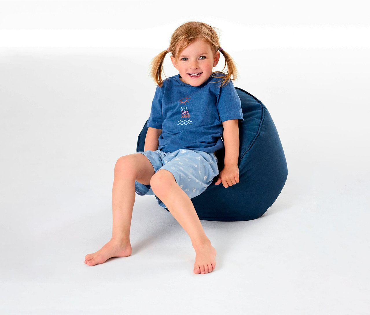 Dziewczynka siedzi na pufie i ma na sobie piżamę dziecięcą SCHIESSER.