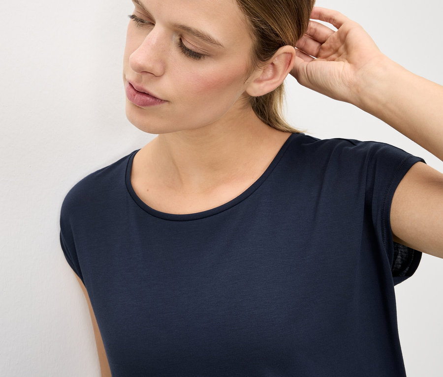 Kobieta w ciemnym T-shircie dotyka ucha.