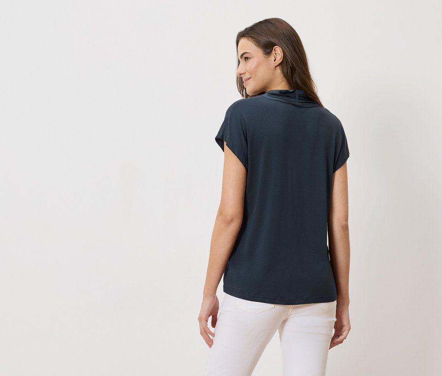 Widok z tyłu kobiety z długimi brązowymi włosami, ubranej w granatową bluzkę i białe dżinsy.