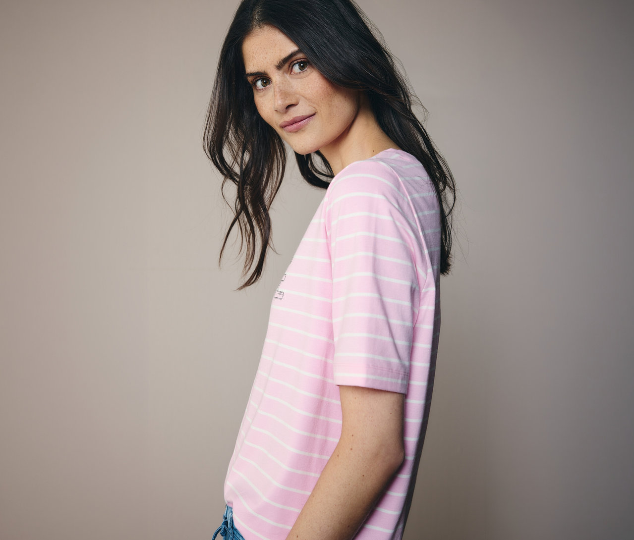 Kobieta patrzy przez ramię, ubrana w różowo-białą koszulkę CECIL w paski.