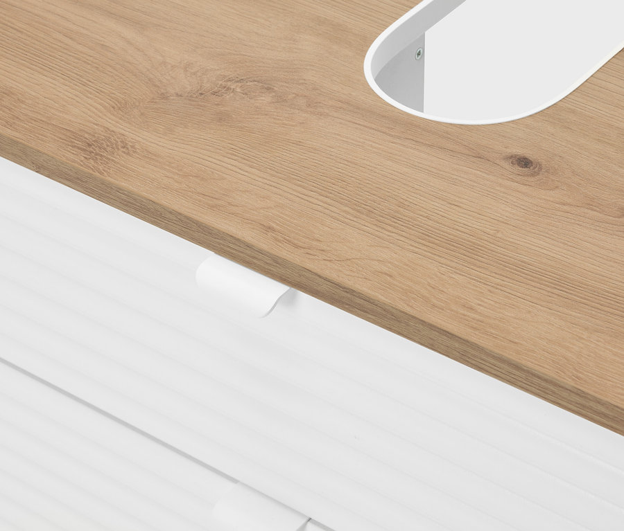 Zbliżenie blatu z jasnego drewna z białym, owalnym wycięciem i białymi szufladami pod spodem.