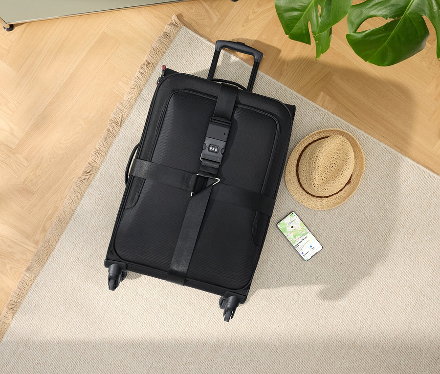 Czarna walizka na kółkach z kapeluszem i smartfonem na beżowym dywanie.