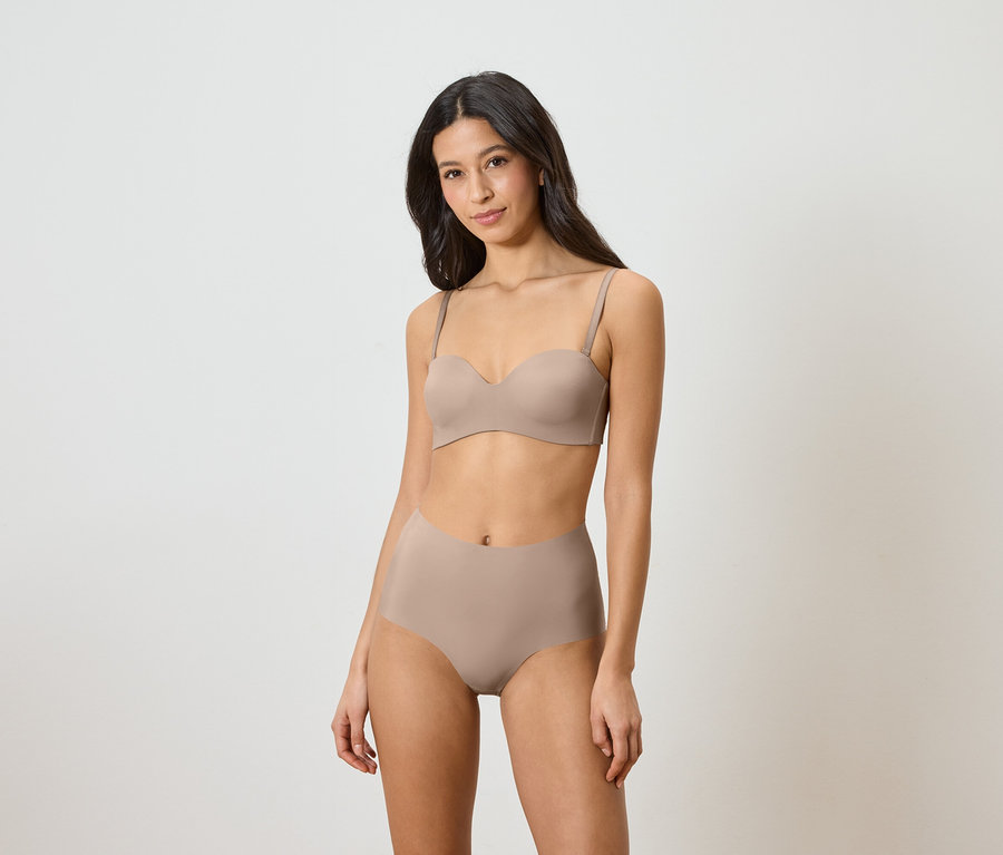 Kobieta ma na sobie beżowy biustonosz bez ramiączek i majtki z wysokim stanem.