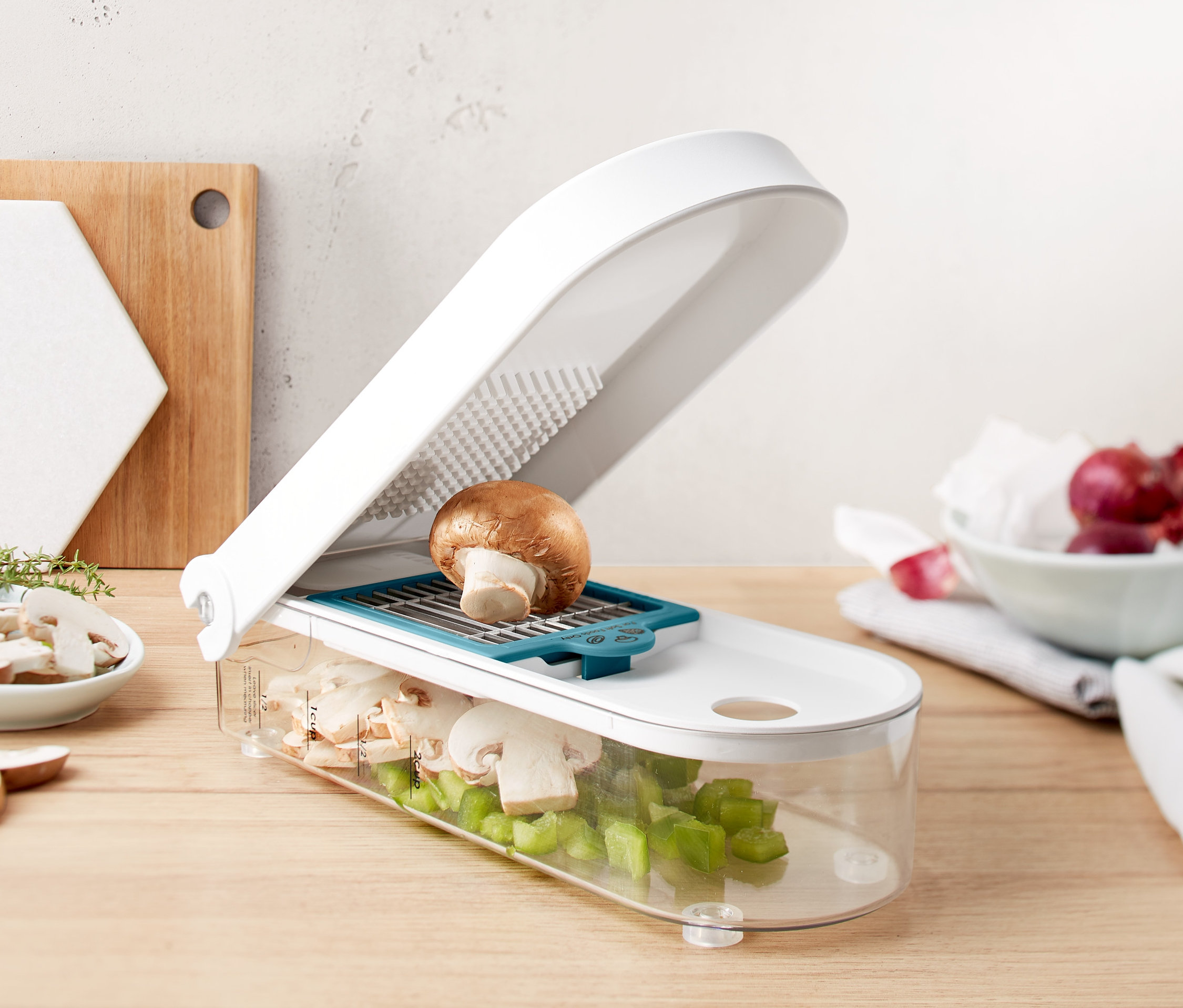 Brązowy grzyb na białej krajalnicy do warzyw i owoców z przezroczystym pojemnikiem wypełnionym pokrojonymi grzybami i zieloną papryką.