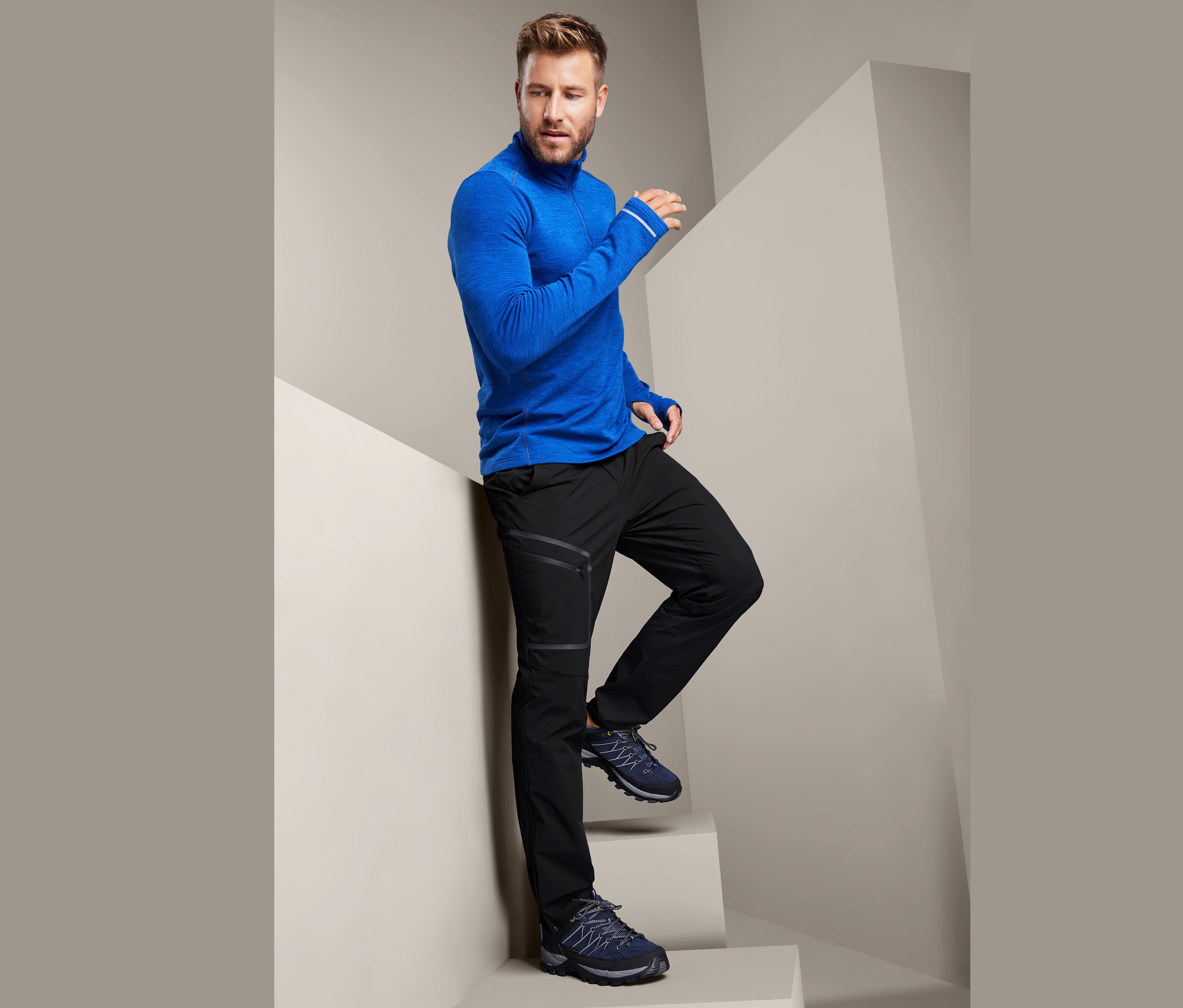 Mężczyzna pozuje na schodach w niebieskiej koszulce sportowej i czarnych spodniach softshell.