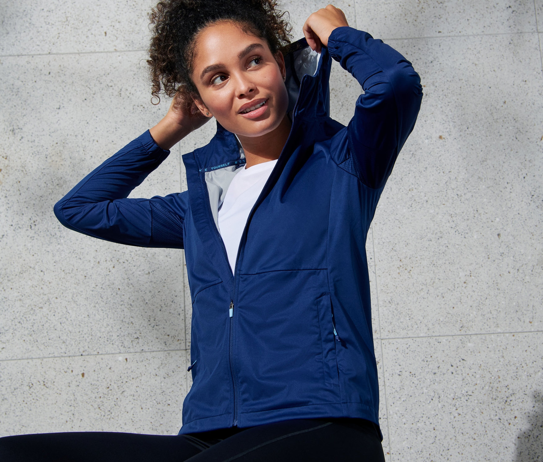 Kobieta poprawia kaptur niebieskiej kurtki do biegania.