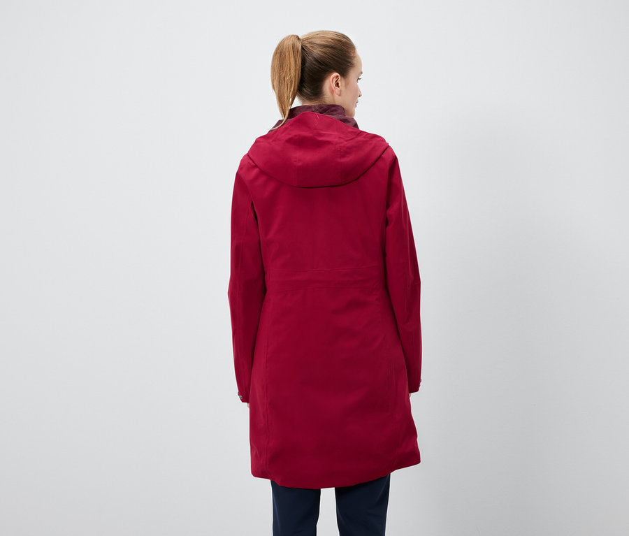 Widok z tyłu kobiety z kucykiem, ubranej w czerwoną kurtkę z kapturem i granatowe spodnie.