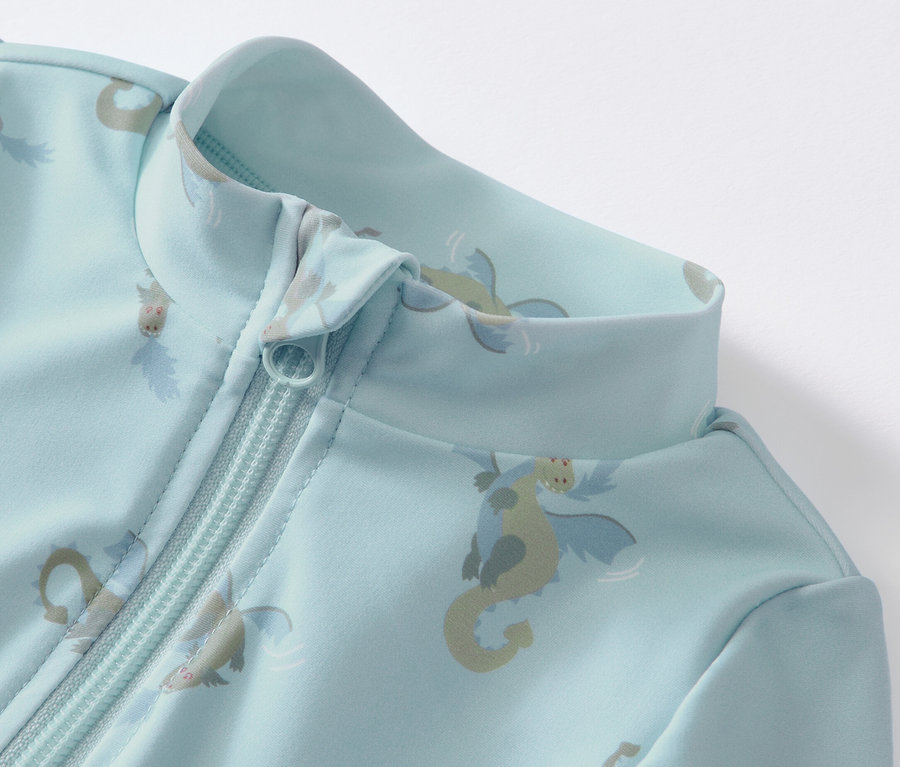 Zbliżenie na niebieski kombinezon niemowlęcy z filtrem UV 80, wzorem smoka i zamkiem błyskawicznym.