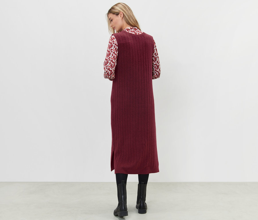 Kobieta stoi tyłem, ubrana w czerwoną sukienkę z prążkowanej dzianiny.