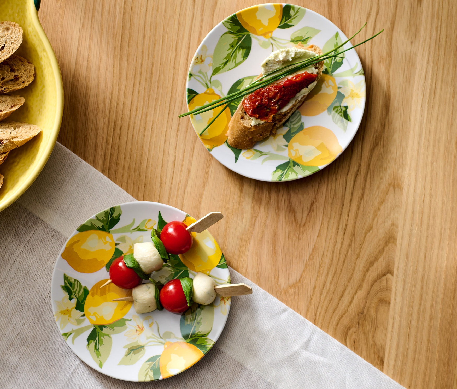 Dwa talerze na przystawki z motywem cytryny, na jednym szaszłyk z pomidorków cherry i mozzarelli.