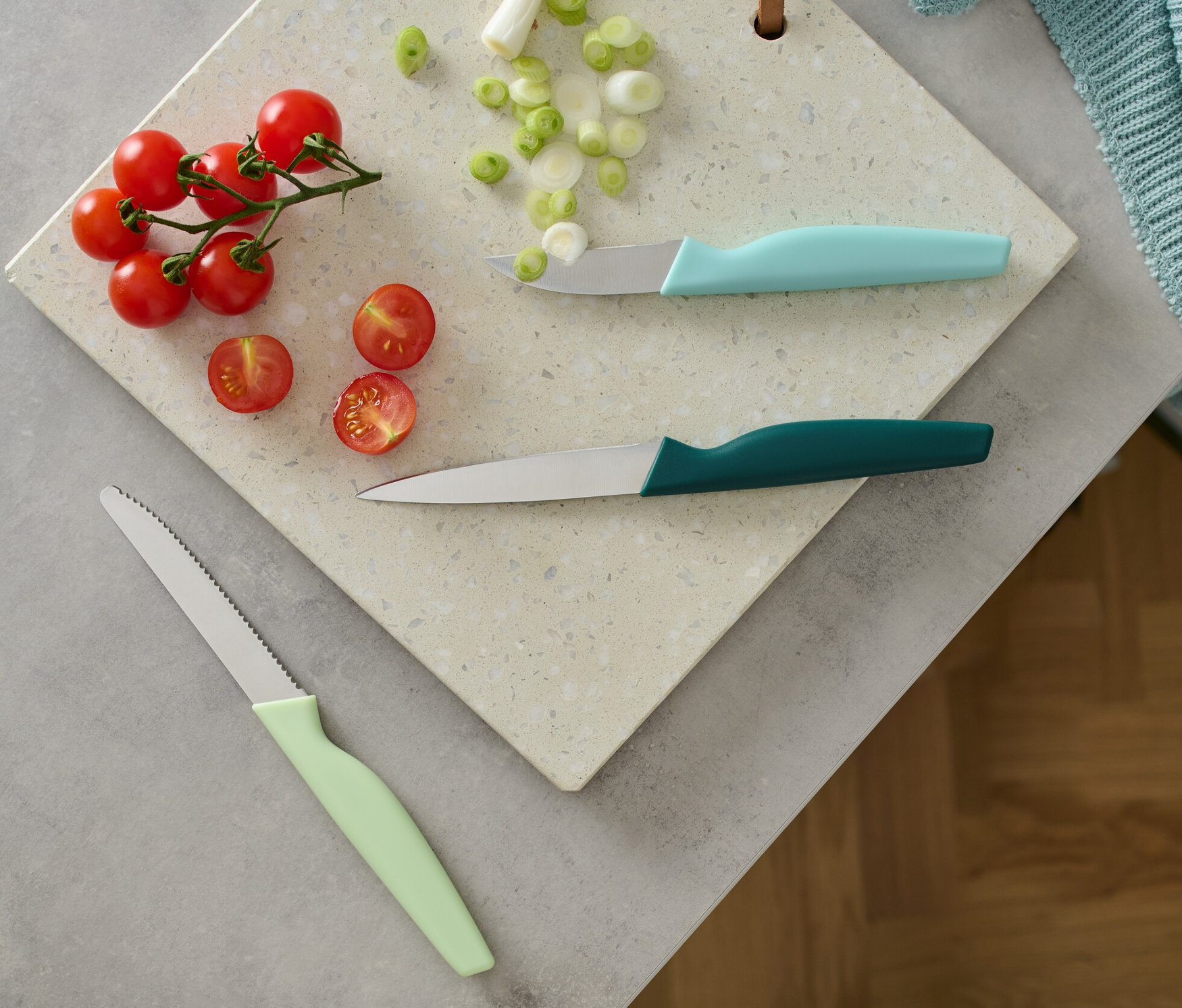 Pomidory, dymka i 3 noże kuchenne na desce do krojenia.