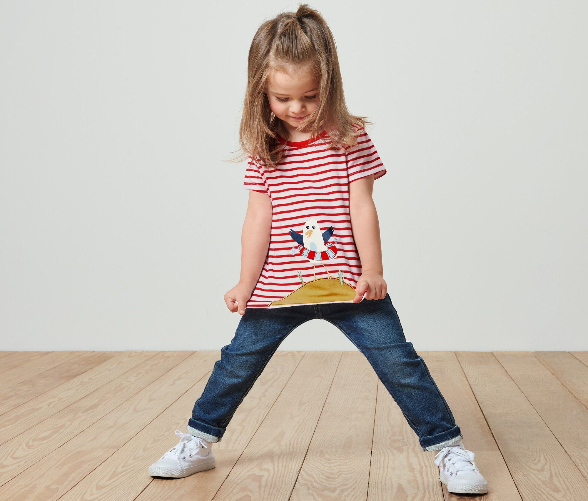 Dziewczyna stoi i trzyma brzeg czerwono-białej koszulki z aplikacją.