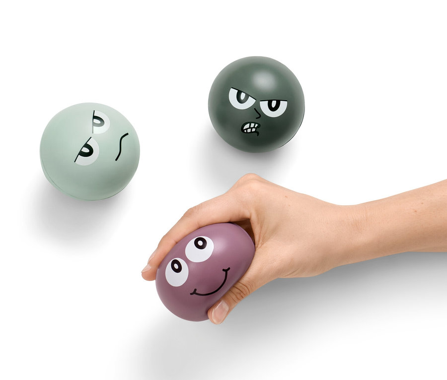 Ręka trzyma fioletową piłkę antystresową, w tle dwie kolejne piłki antystresowe.