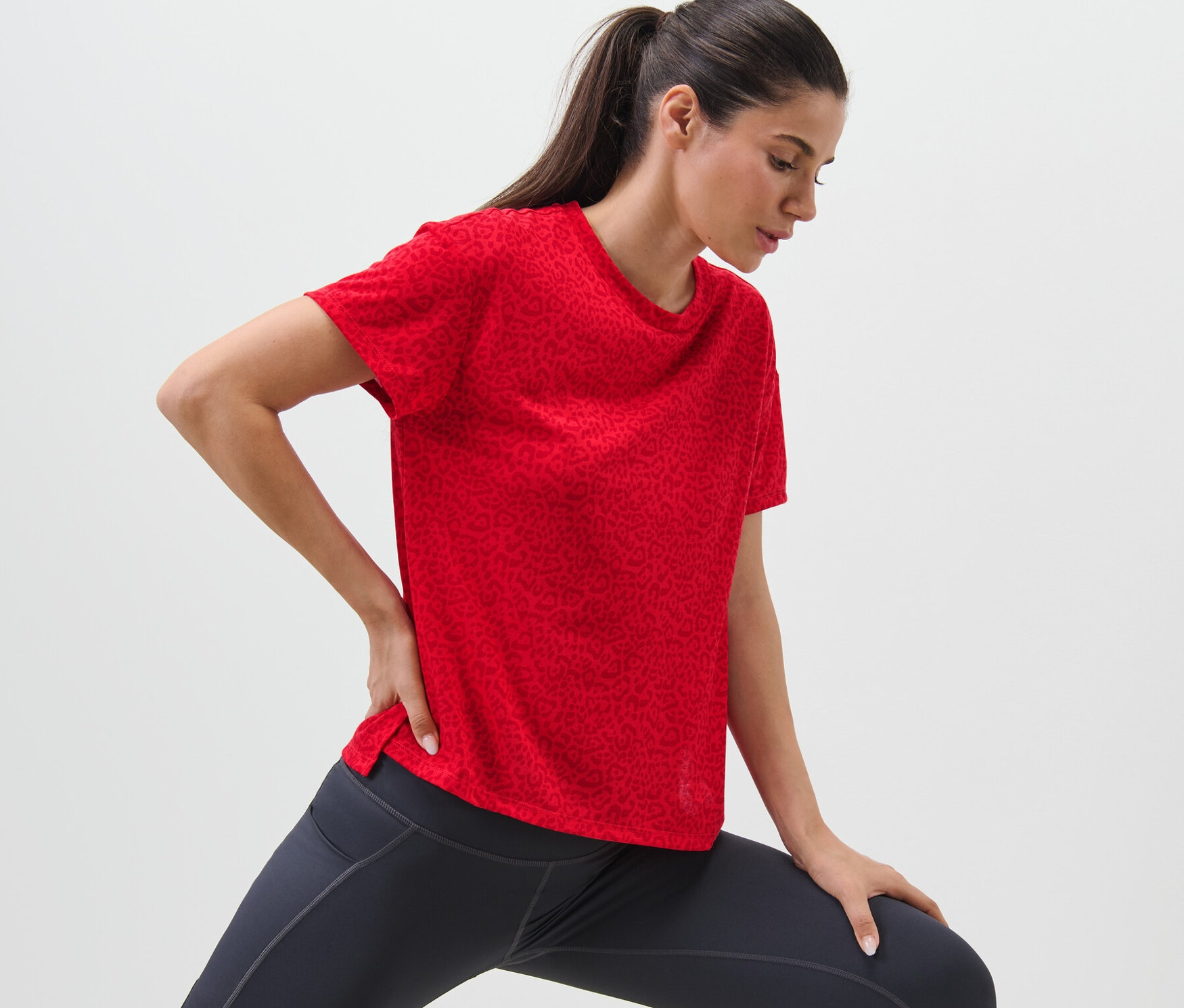 Kobieta rozciąga się w czerwonej koszulce sportowej.