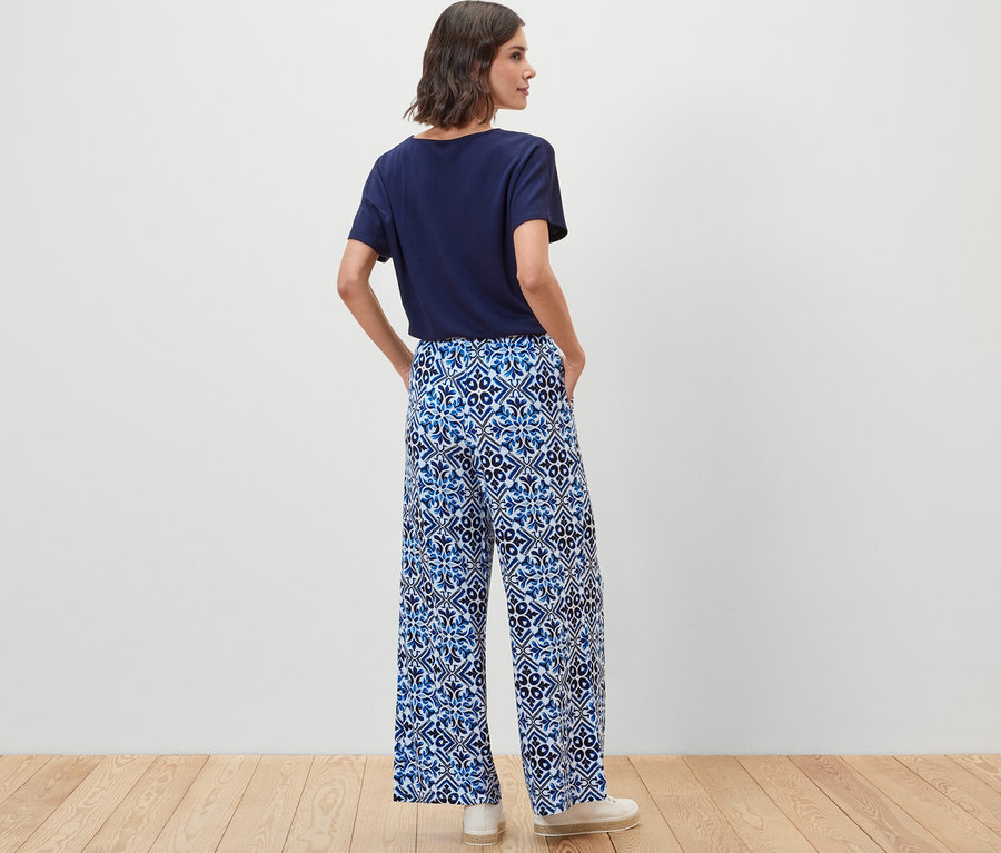 Kobieta stoi tyłem, ubrana w granatowe, wzorzyste spodnie palazzo.