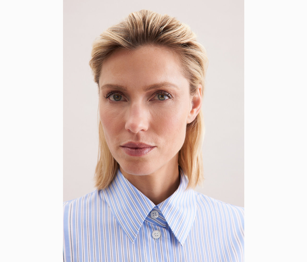 Portret kobiety o blond włosach w koszuli oversize Seidensticker w niebiesko-białe paski.