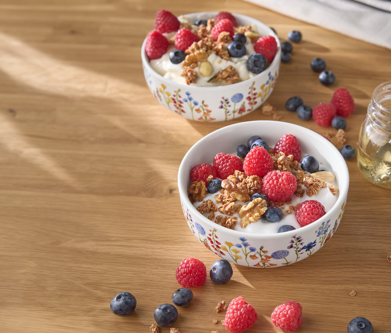 Dwie miski jogurtu z malinami, jagodami i orzechami na drewnianym stole.