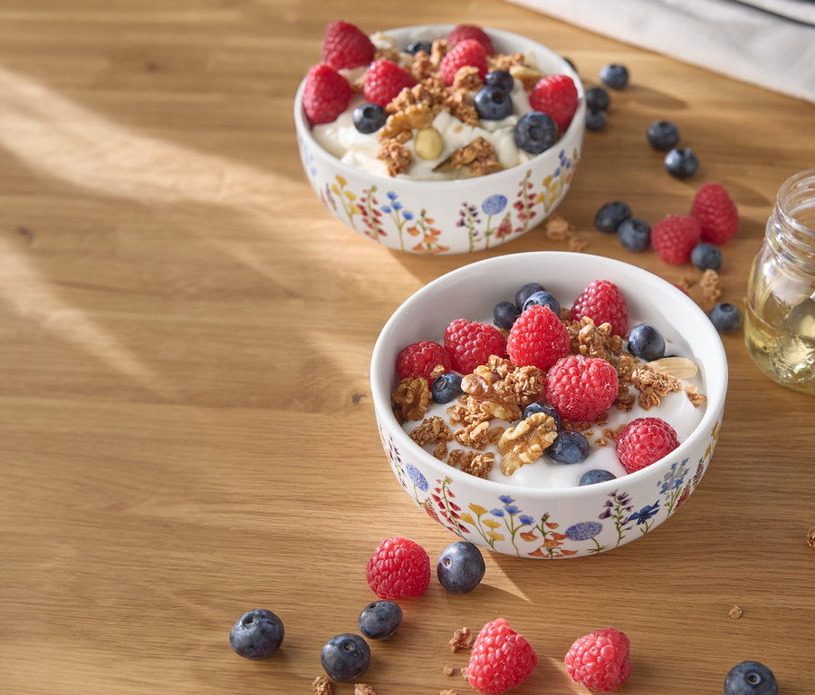 Dwie miski jogurtu z malinami, jagodami i orzechami na drewnianym stole.