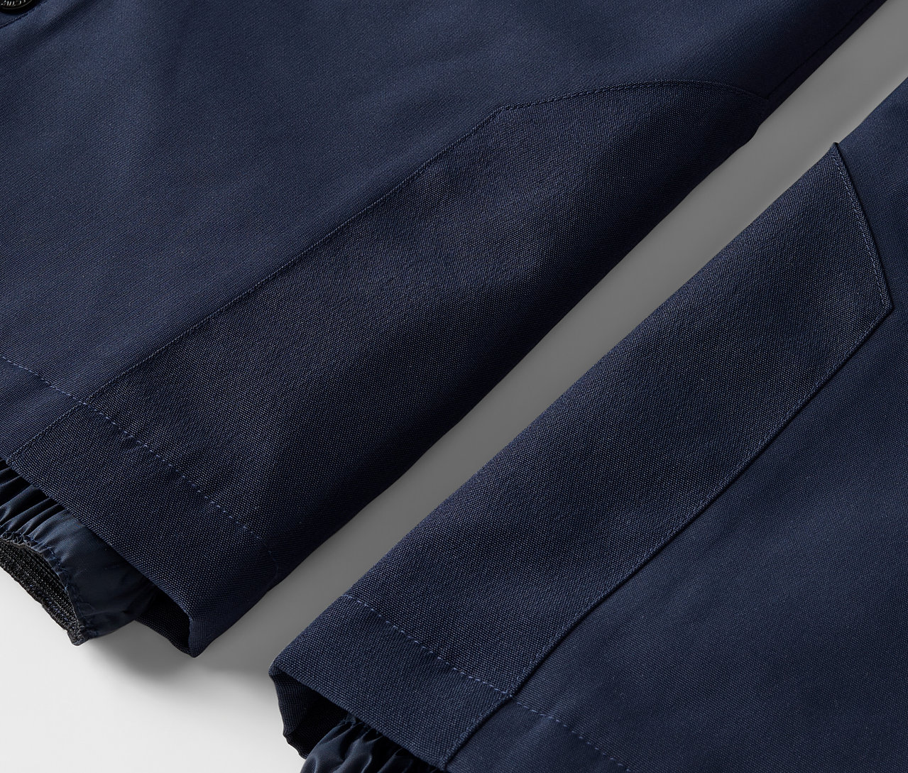 Zbliżenie na dwie nogawki granatowych spodni z elastycznymi mankietami.